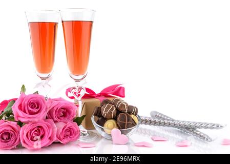 Valentine's Day concept. Two glasses of wine, gift box, candles, pink roses, sponge satin hearts and delicious chocolate pralines on a white backgroun