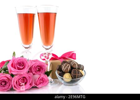 Valentine's Day concept. Two glasses of wine, gift box, pink roses and delicious chocolate pralines on a white background with copy space for text. Se Stock Photo