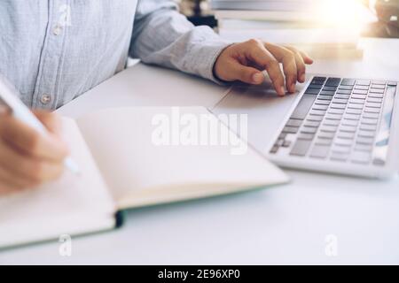 Woman is writing in planner notebook while using laptop to work or plan with workspace at home. Education business lifestyle concept. Stock Photo