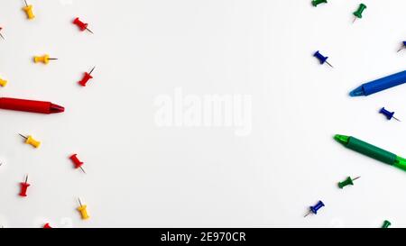 Yellow red blue green push pins and pens at the left and right on white background. Flat lay top view. Education back to school and online study conce Stock Photo