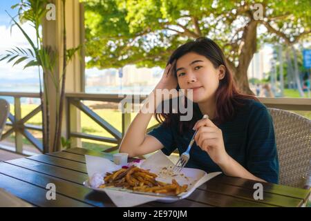 Biracial teen girl eating french fries at outdoor restaurant near ocean in Hawaii Stock Photo