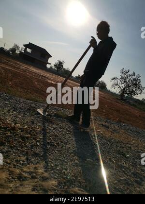 Silhouette of an old man holding a hoe on the vacant land before cultivation. Stock Photo