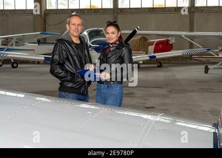 Flight Instructor Talking to Female Trainee Pilot. Woman and Man Standing Next to Small Planes in Airport Hangar. Stock Photo