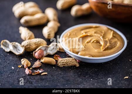 Peanut butter in bowl and peanuts on black table. Stock Photo