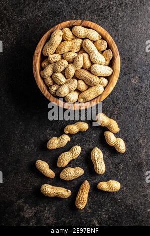 Dried peanuts. Tasty groundnuts in bowl on black table. Top view. Stock Photo