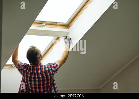 For a better view. Rear view of handyman using measure tape while measuring a window in a new dry wall attic Stock Photo