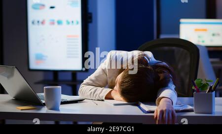 Freelancer working overtime on project falling asleep on desk with hand on financial documents trying to respect the deadline. Employee using modern technology network wireless, sleeping on table. Stock Photo