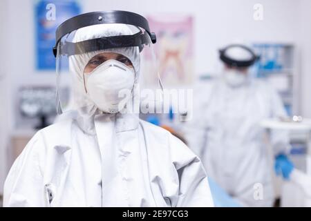 Dentist looking exhausted at camera dressed in coverall in the course of covid-19 pandemic. Portrait of tired stomatologist wearing coronavirus ppe suit looking at camera. Stock Photo