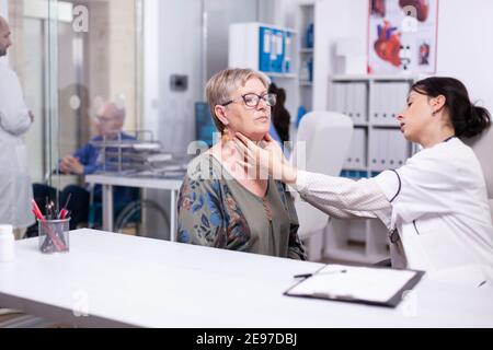 Professional physician checking neck lymph nodes of old woman, palpating senior woman. Elderly patient visiting doctor at hospital examining thyroid throat touching health at clinic, treatment medical Stock Photo