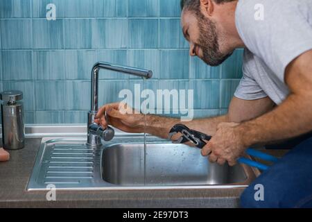 Fix a leak. Close up shot of professional repairman using pipe wrench while examining and fixing faucet in the kitchen Stock Photo