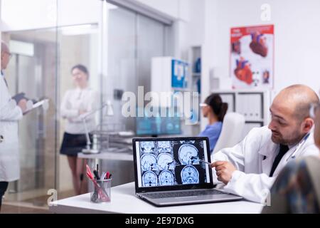 Woman speaking with doctor during consultation about cerebral x-ray using laptop in hospital. Senior patient visiting physician telling health complaints, medical practitioner explaining treatment. Stock Photo