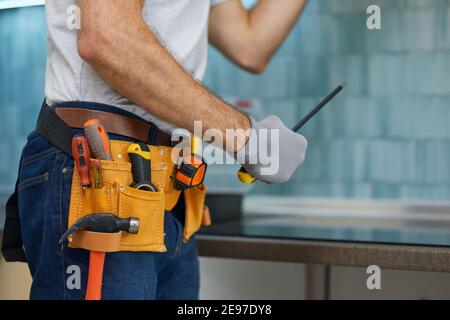 Expert. Cropped shot of young repairman, professional plumber holding a screwdriver while fixing a sink in the kitchen indoors Stock Photo