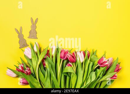 Easter card with pink and red tulips and wooden bunny on yellow background.  Stock Photo