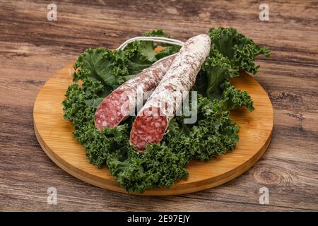 Spanish Fuet sausage with salad leaves over wooden background Stock Photo