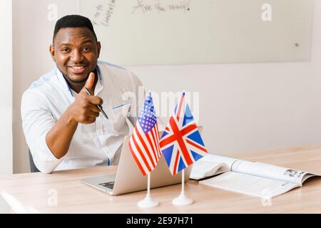 English and British flags in front. Black handsome translator uses his laptop for online work according social distancing. Scientist works at home on Stock Photo