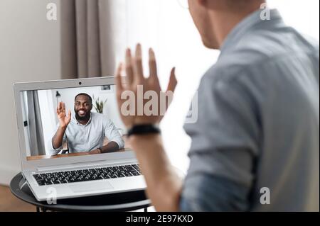 Two employees talking online via video call. A young guy waving hello to an African-American man on the laptop screen, online video meeting, video Stock Photo