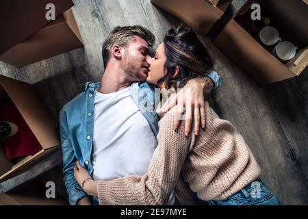 Husband and wife kissing lying on the floor at home - Young couple just moved into new apartment - People and relocation concept. Stock Photo
