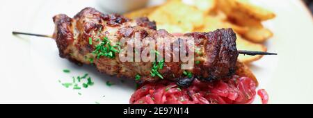 Close-up of delicious fresh baked meat and crusty potato served on white plate. Tasty dish decorated with greenery. Red yummy sauce. Portion for one. Stock Photo