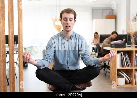 Handsome man meditating while sitting crossed legs on a chair in the office. Stock Photo