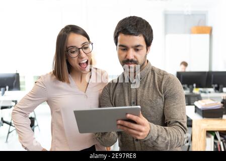 Hispanic proud man showing something to a surprised coworker on his tablet at the office. Stock Photo