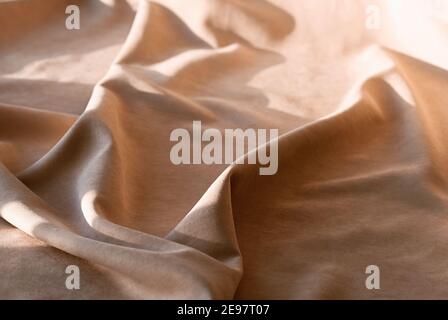 Beige linen fabric with pleats. Abstract neutral textile background. Selective focus. Close up. Stock Photo