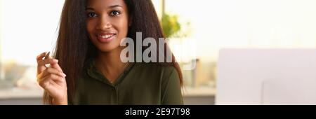 Smiling african woman sitting in office holding notebooks and pen Stock Photo