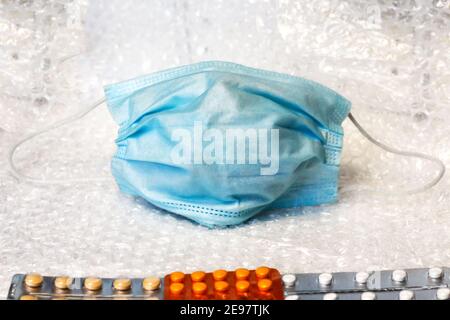 A metaphor of a face in a blue medical mask looks at blisters of different pills. Virus and pandemic. Selective focus Stock Photo