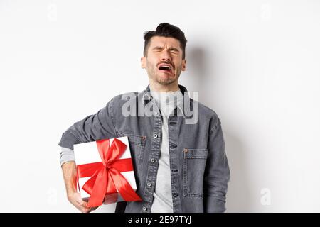 Valentines day heartbreak. Single and heartbroken guy crying lonely, holding big gift box, being rejected by lover, sobbing and feeling alone Stock Photo