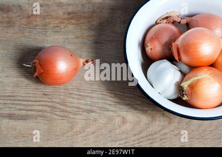 old fashioned still life with onion and garlic in enamel bowl on rustic wood Stock Photo