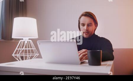 Caucasian man using laptop at home with cup of coffee nearby. High quality photo Stock Photo