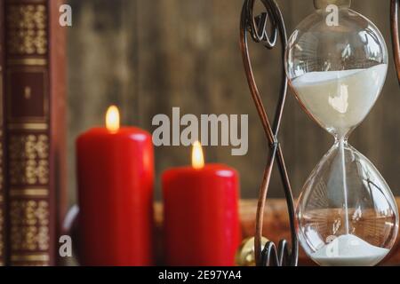 Hourglass and red burning candles close up