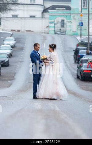 the bride and groom on the background of a church, religious lovers, a wedding walk in winter, a man and a woman gently kiss and smile hugging Stock Photo