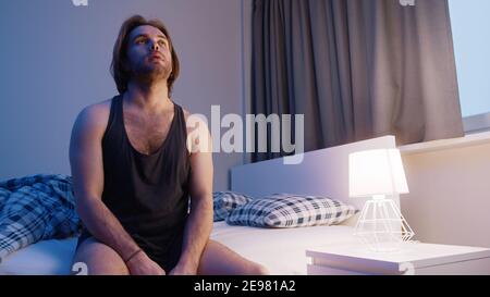Young caucasian man sitting on the bed . Insomnia problem, mental disorder or depression. High quality photo Stock Photo