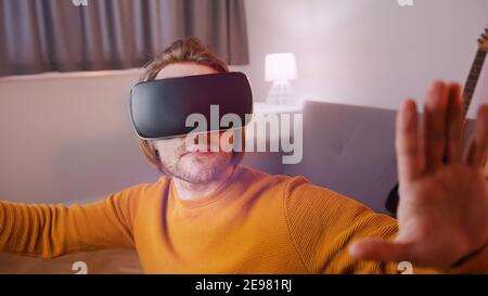 Virtual reality. Young man with VR set in his appartment, Guitar in the background. High quality photo Stock Photo