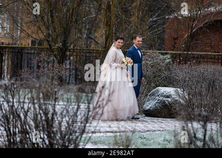 the bride and groom on the background of a church, religious lovers, a wedding walk in winter, a man and a woman gently kiss and smile hugging Stock Photo