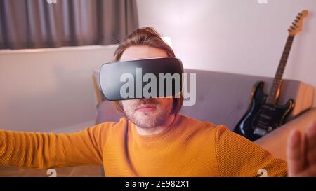 Virtual reality. Young man with VR set in his appartment, Guitar in the background. High quality photo Stock Photo