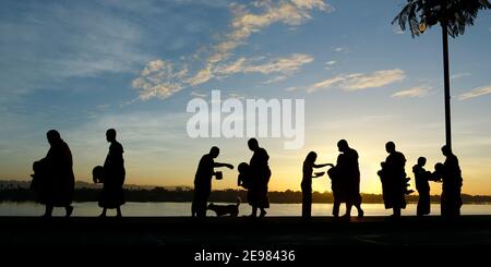 silhouette of monks dressing orange robe during reception of alms, on the shore of the mekong river Stock Photo