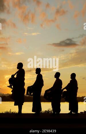 silhouette of monks dressing orange robe during reception of alms, on the shore of the mekong river Stock Photo