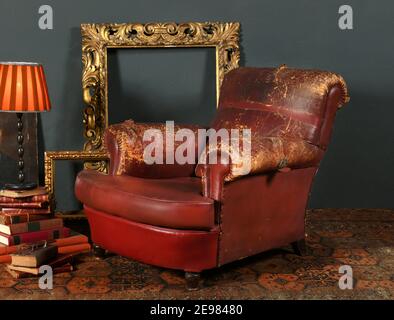 Old shabby red leather armchair placed near vintage decorative frames and lamp in room with retro style interior Stock Photo