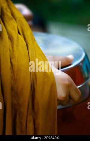 hand of monk dressing orange robe, holding bowl during reception of alms, around buddhist temple Stock Photo