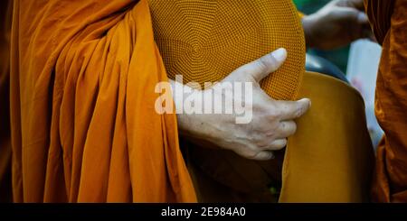 hand of monk dressing orange robe, holding bowl during reception of alms, around buddhist temple Stock Photo