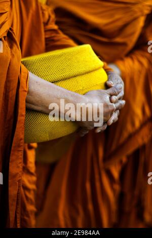 hand of monk dressing orange robe, holding bowl during reception of alms, around buddhist temple Stock Photo