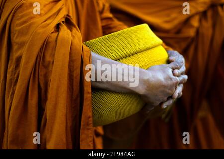 hand of monk dressing orange robe, holding bowl during reception of alms, around buddhist temple Stock Photo