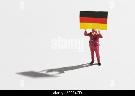 Miniature toy figure of female character carrying German flag on white background with shadow Stock Photo