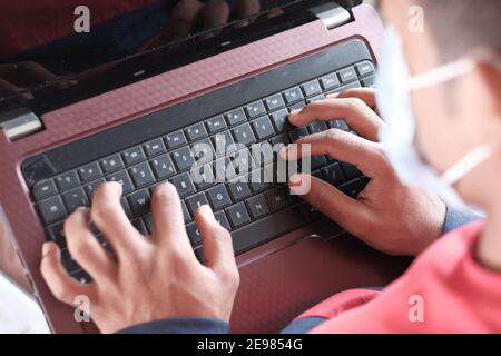 side view of young man in surgical mask using laptop at home  Stock Photo