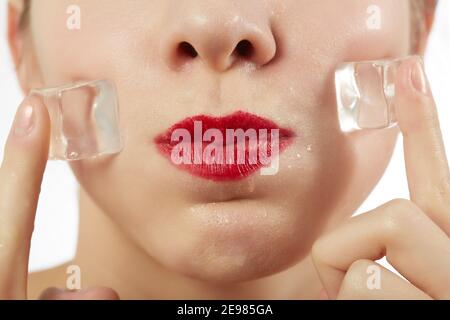 serious young woman applying ice cubes on her face skin on white background Stock Photo