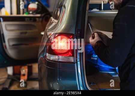 Mechanic repairing car rear light. Electromechanical workshop. Working with his hands. Tools. Concept of car repair Stock Photo