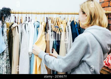 Woman shopper chooses fashionable clothes on hangers in a boutique. Stock Photo