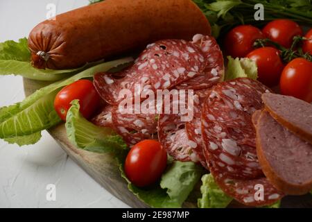 A selection of spicy dried or smoked  sausages on lettuce leaves with cherry tomatoes Stock Photo