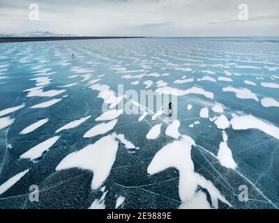 Aerial view drone shoot of group of people at bicycle riding on the frozen lake with mountains at background Stock Photo